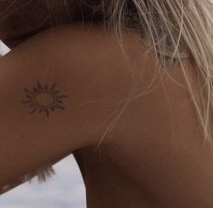 the back of a woman's shoulder with a small sun tattoo on her left arm