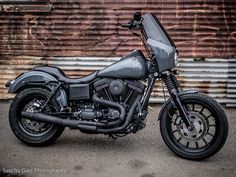 a black motorcycle parked in front of a metal building with graffiti on the wall behind it