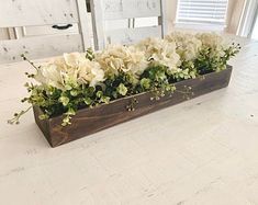 a wooden planter filled with white flowers on top of a table next to a window