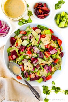 a white bowl filled with salad next to two bowls of dressing and sliced radishes