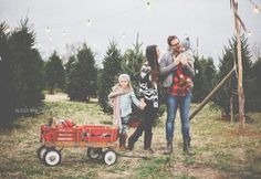 a man and two children are pulling a red wagon with christmas trees in the background