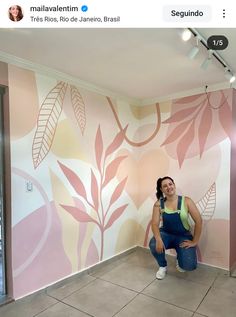 a woman squatting on the ground in front of a wall with leaves painted on it