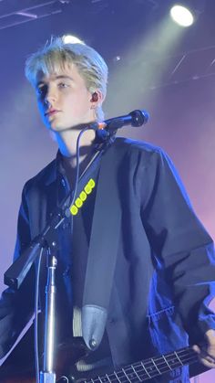 a young man holding a guitar while standing in front of a microphone on top of a stage