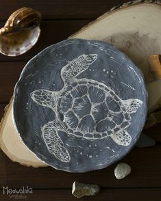 a ceramic plate with a sea turtle on it next to shells and seashells