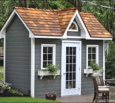 a small gray shed with two windows and a brown roof