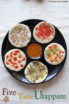 four small pizzas on a black plate with sauce and condiments in the middle