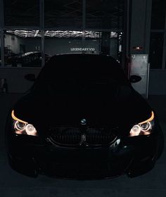 the front end of a black car with its lights on in a dark garage area