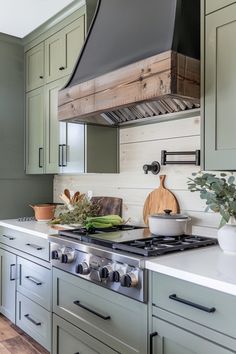 a stove top oven sitting inside of a kitchen next to green cupboards and drawers