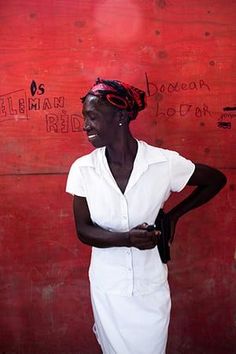 a woman is standing in front of a red wall with writing on it and smiling