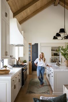 a woman standing in the middle of a kitchen with white cabinets and wood floors, while looking at the camera