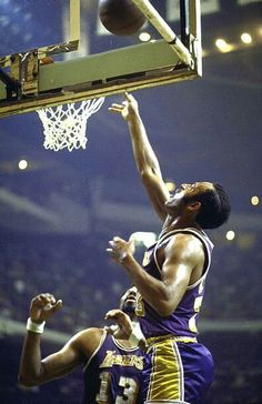 two men playing basketball against each other in the air with one reaching for the ball