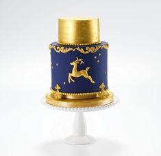 a blue and gold decorated cake sitting on top of a white pedestal