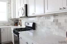 a kitchen with white cabinets and marble counter tops, along with a black stove top oven