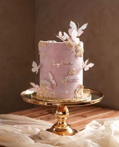 a pink and gold cake with butterflies on it sitting on top of a wooden table