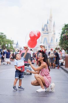 a woman kneeling down next to a little boy holding a balloon in front of a castle