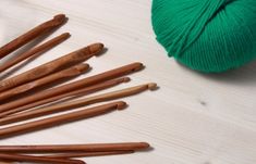 a green ball of yarn next to several wooden crochet hooks