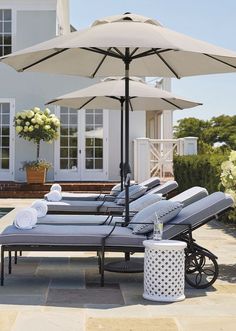 lounge chairs and an umbrella near a swimming pool in front of a large white house