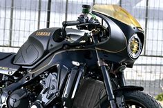 a black and gold motorcycle parked in front of a metal fence with it's lights on