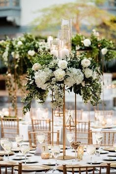 an elegant centerpiece with white flowers and greenery is displayed on a gold stand