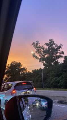 the rear view mirror of a car with trees in the back ground and sunset behind it