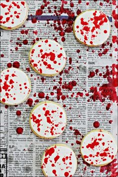 some cookies with red splatters are on top of a newspaper page and it is covered in white icing