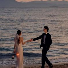 a bride and groom holding hands on the beach at sunset with mountains in the background