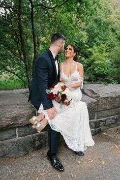 a bride and groom sitting on a stone wall