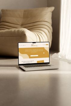 an open laptop computer sitting on top of a wooden table next to a white couch