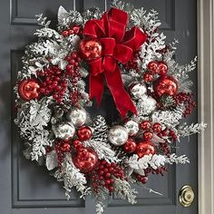 a christmas wreath with red and silver ornaments hanging on the front door to welcome guests