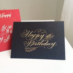 two happy birthday cards sitting on top of a white table next to red and black greeting cards