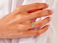 a woman's hand with a diamond ring on her left hand, wearing a white shirt