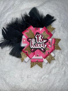 a pink and gold brooch with black feathers on it's side that says 13th birthday