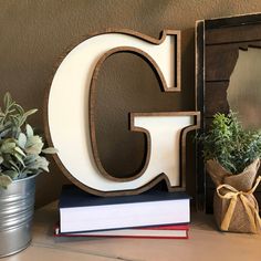 a wooden letter sitting on top of a table next to a potted plant and books