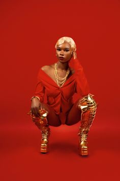 a woman sitting on the ground with her legs crossed, wearing gold shoes and a red top