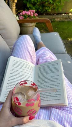 a person laying down reading a book and drinking a drink