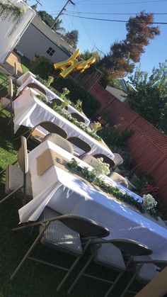 there are many tables and chairs set up in the yard with white tablecloths on them