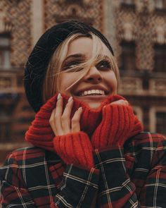 a woman with blonde hair wearing a red sweater and black beanie smiles at the camera