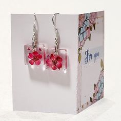 a pair of pink flower earrings sitting on top of a white box next to a card