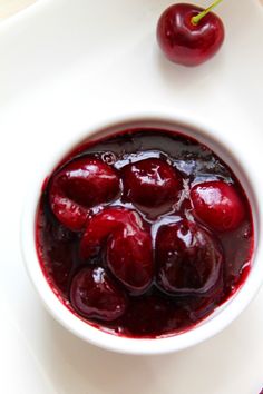 a bowl filled with cherries sitting on top of a white table next to an orange