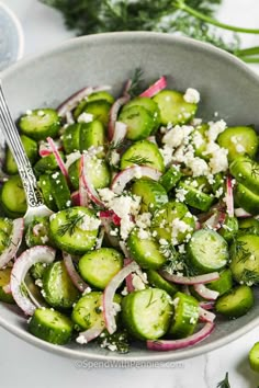 a bowl filled with cucumbers, onions and feta cheese topped with herbs