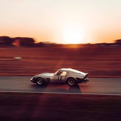 an old race car driving down the road in front of the setting sun on a clear day