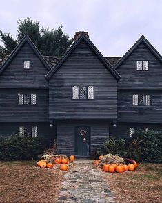 an old black house with pumpkins in the front yard and stone walkway leading up to it