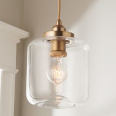 a clear glass light fixture hanging from a white wall with a gold colored metal fitting