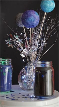 a vase filled with blue and purple balls sitting on top of a table next to two jars