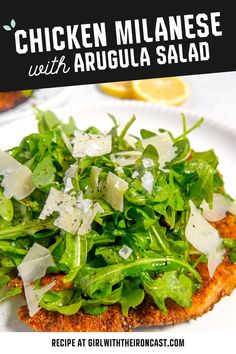 chicken with arugula salad on a white plate next to lemon wedges and parmesan cheese