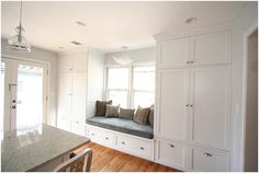 a kitchen with white cabinets and a window seat in the center, along with a marble counter top