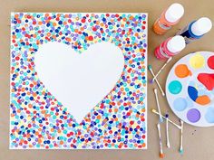 an art project with paint and craft supplies on the table, including a paper heart