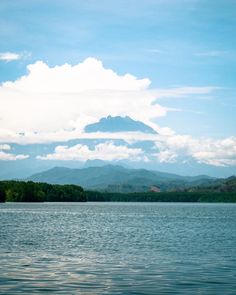 a lake with mountains in the background under a blue sky filled with white fluffy clouds