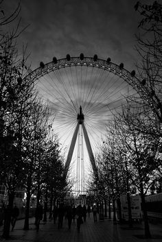 black and white photograph of the london eye at night with people walking in front of it