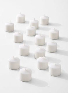 many white candles are arranged in the shape of a triangle on a white surface with shadows